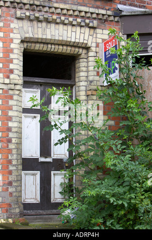 Vieille porte fenêtre cassée et envahi par le jardin avant de la vieille maison mitoyenne avec vendu enseigne à l'extérieur Banque D'Images