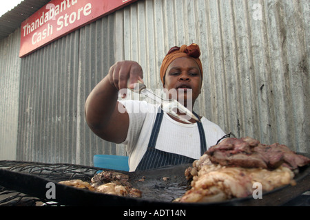 Foies de mouton frites femme plus de charbons ardents sur le trottoir à l'extérieur d'une boutique, canton, près de Phillipi Khayelitsha, Cape Town. Banque D'Images