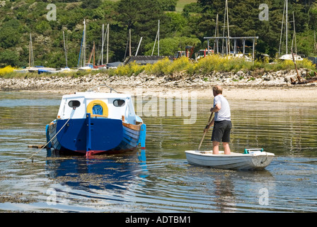 Carrick Roads à St juste dans Roseland style de vie vue arrière homme dans un petit dingue et pagayant pour aller à la cabine amarrée bateau cruiser au-delà de Cornwall Angleterre Royaume-Uni Banque D'Images