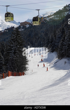 Skieurs sur les pistes bordées d'un livre vert s'exécutent comme téléphériques passent au-dessus de Méribel dans le domaine skiable des Trois vallées des Alpes Françaises Banque D'Images