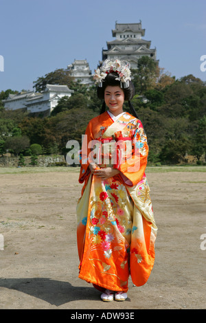 Jeune japonaise portant un kimono traditionnel orange pose en face de Himeji castle Kansai Japon Asie Banque D'Images