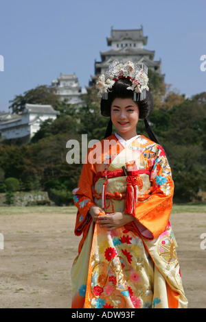 Jeune japonaise portant une robe traditionnelle de couleur orange vif vif pose en face de château de Himeji au Japon Asie Banque D'Images