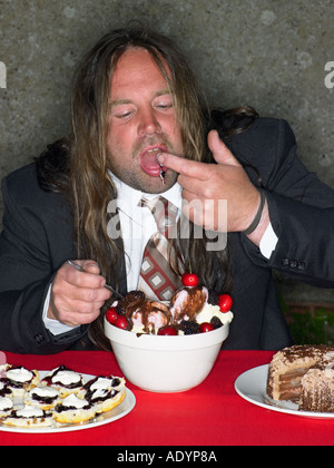 Gros homme aux cheveux longs manger bouche lui-même avec du gâteau et de la crème glacée Banque D'Images