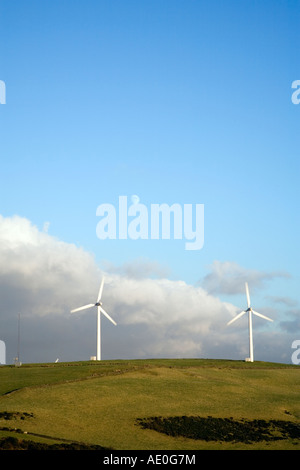 Flanc de coteau rural montrant deux éoliennes contre un ciel bleu avec un peu de nuage et la lune Banque D'Images