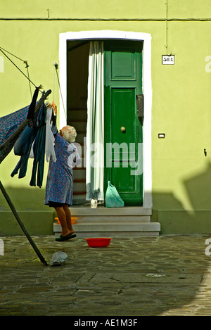 Une vieille dame pend son linge à l'extérieur une maison verte Banque D'Images