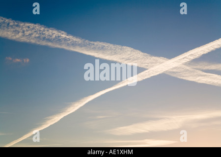 Des pistes de vapeur d'avion sillonnent une soirée où le ciel est bleu clair Banque D'Images