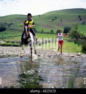 Une femme en marche et un cheval galopant à travers la Abergwesyn Ford à l'homme par rapport à course de chevaux Llanwrtyd Wells Wales UK KATHY DEWITT Banque D'Images