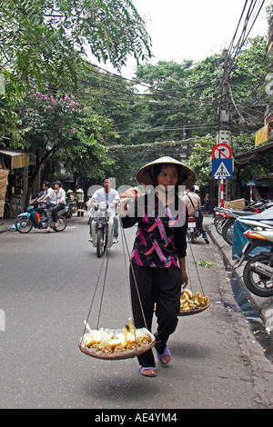 Femme à pied en vente chapeau conique les bananes et morceaux d'ananas de l'épaulement pannier baskets Vieux Quartier Hanoi Vietnam Banque D'Images