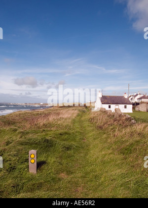 ANGLESEY SENTIER CÔTIER et blanc Tyntwyn Cottage, Bwthyn Tyn Towyn, à Porth Nobla avec Rhosneigr Beyond. Île d'Anglesey, Pays de Galles, Royaume-Uni, Grande-Bretagne Banque D'Images