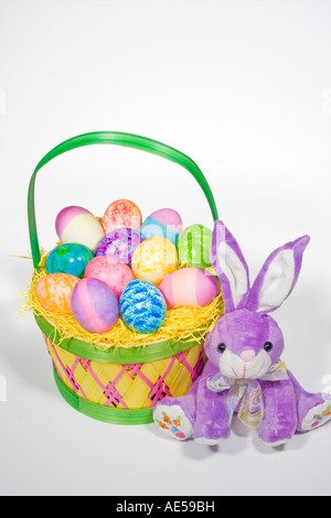 Panier de Pâques de paille rempli d'oeufs de différentes couleurs et de motifs avec lapin en peluche mauve Banque D'Images