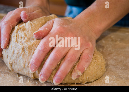 Mains le pétrissage du pain de blé entier pâte sur une planche à découper en bois Banque D'Images