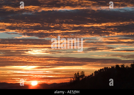 Soleil au-dessus des collines illuminant le ciel avec nuages orange brillant Banque D'Images