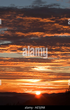 Soleil au-dessus des collines illuminant le ciel avec nuages orange brillant Banque D'Images