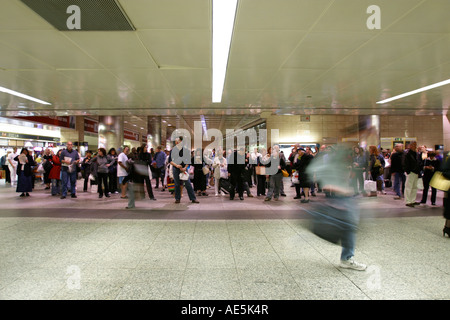 Les gens debout dans la salle d'attente de Penn Station à la recherche jusqu'à l'horaire des trains que l'homme se précipite pour attraper son train par Banque D'Images