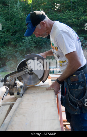 Carpenter dans ses mi 50s abaisse le bras de scie composé de couper une pièce de bois sur un site de construction Banque D'Images