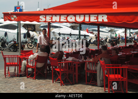 Serveur & clients à la populaire pâtisserie Senequier et bar rouge sur le trottoir du front de mer avec des lancements de bateaux à moteur au-delà de St Tropez Sud de la France Banque D'Images