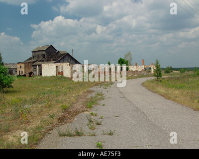 Vue sur route ouverte avec des propriétés en décomposition à l'abandon en zone d'exclusion de Tchernobyl Bélarus Banque D'Images