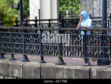 Couverture de jeune fille musulmane portant un foulard bleu, en utilisant un téléphone cellulaire, Riverfront, Sungai Sarawak River, Kuching, Malaisie, Bornéo Banque D'Images