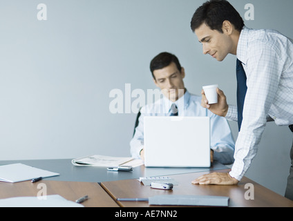 Businessman leaning on table avec tasse en main pendant que collègue utilise coffre Banque D'Images