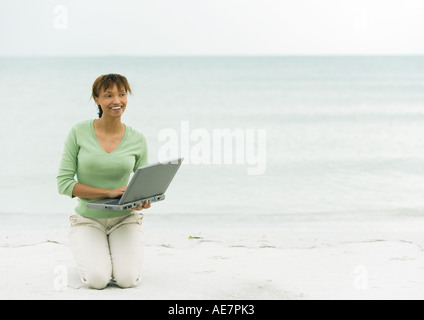 Woman on beach, à genoux sur le sable avec l'ordinateur portable Banque D'Images
