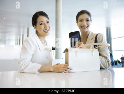 Deux businesswoman smiling, un sac à main de portefeuille, l'autre tenant du passeport Banque D'Images