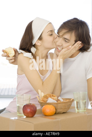 Couple having breakfast sur carton fort, woman kissing man's cheek Banque D'Images