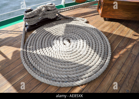 Une lourde ligne d'amarrage soigneusement enroulée dans une spirale plate (une bobine flamande) sur le pont en teck du grand voilier équatorien Guayas, à côté d'une borne - Cagliari, Sardaigne, Italie. Banque D'Images