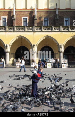 Petit garçon rss les pigeons à l'extérieur de la Halle Place du marché, Cracovie, Pologne. Banque D'Images