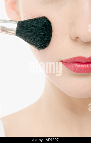 Jeune femme visage avec Make-Up, tenant un pinceau devant elle, close-up (studio) Banque D'Images