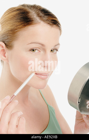 Jeune femme faisant face à sa bouche avec un stylo, petit miroir dans sa main, close-up (studio) Banque D'Images