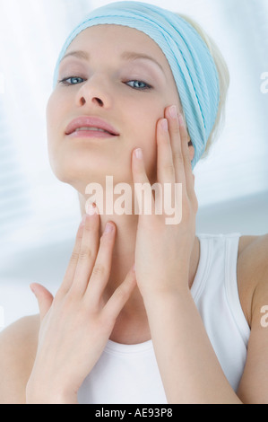 Jeune femme regardant la caméra, posant ses mains sur son cou close-up (studio) Banque D'Images