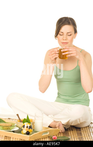 Jeune femme assise sur un tapis de bambou, tasse de thé vert potable Banque D'Images