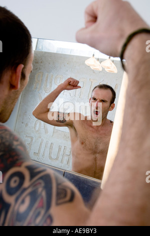 Tattooed man flexing muscles en face de miroir de salle de bains Banque D'Images