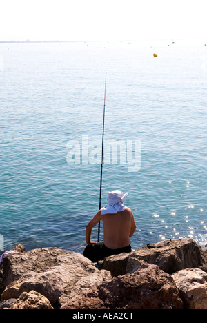 Un homme seul pêcheur à tête sur tshirt est assis sur des rochers en attente pour le poisson de mordre Banque D'Images