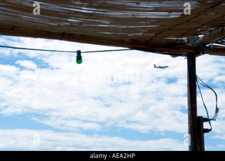 Un détail d'une des ampoules verte suspendue à un toit de paille dans un bar de plage avec un avion voler en arrière-plan Banque D'Images