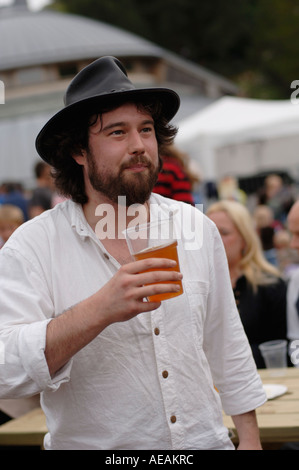 Homme barbu portant un chapeau de boire une pinte de bière blonde d'un verre en plastique, UK Banque D'Images