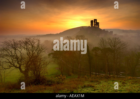 Château de corfe castle à l'abandon près de swanage dorset avec l'éclairage orangé de l'aube dans le ciel et brouillard tourbillonnant dans la vallée Banque D'Images