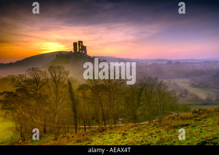 Château abandonné à Corfe Castle Dorset avec l'éclairage orangé de l'aube dans le ciel et brouillard tourbillonnant au-dessus du village Banque D'Images