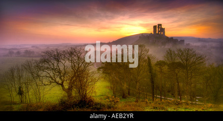 Château de Corfe Castle à l'abandon près de Swanage Dorset avec l'éclairage orangé de l'aube dans le ciel et brouillard tourbillonnant dans la vallée Banque D'Images