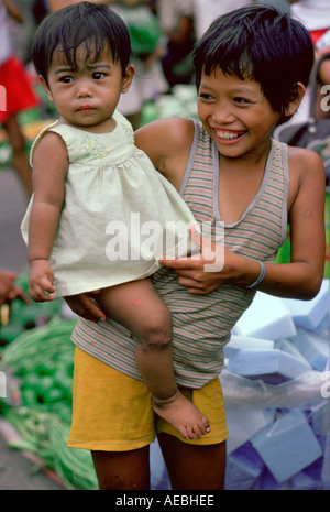 Jeune garçon portant sa sœur à travers le marché de Manille aux Philippines Banque D'Images