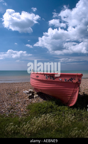 Bateau rouge sur une plage de galets avec beau ciel bleu Banque D'Images