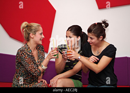 Trois jeunes femmes dans un bar un soir d'augmenter leurs verres dans un toast Banque D'Images