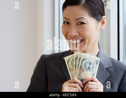 Middle-aged Asian businesswoman holding billets yen Banque D'Images