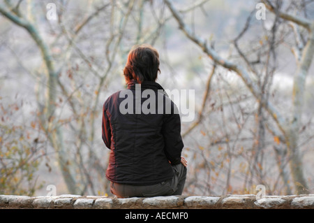 Femme d'âge moyen assis sur le mur donnant sur la brousse africaine Banque D'Images