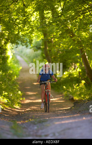 Femme en vtt le vélo vers le bas pays verdoyant lane nr enfant Okeford Dorset England UK Banque D'Images