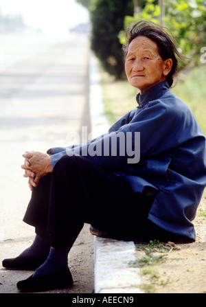Vieille Femme assis sur le bord de la route avec les pieds liés en 1990 Banque D'Images