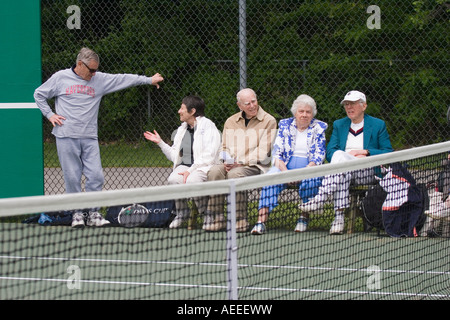 Les hommes âgés et les femmes assises sur les bancs à côté d'un court de tennis à regarder un match en cours et le chat Banque D'Images