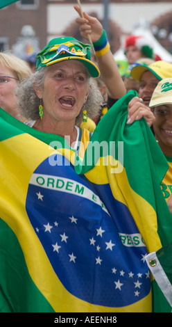 Une vieille femme fan de football brésilien tenant une bannière brésilien tout en chantant son hymne national Banque D'Images