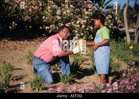 Fillette de 7 à 9 ans qui donne un jus d'orange fruits a embauché pour aider grand-père Grand-père Père jardinage Jardins travailleur retour POV de cour avant Banque D'Images