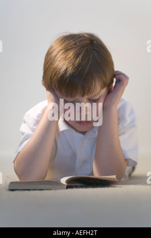 Un jeune écolier dans une profonde concentration lire un livre Banque D'Images